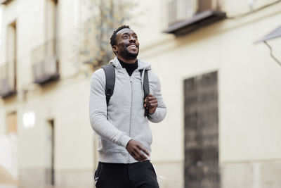 Young man with backpack looking away while walking outdoors