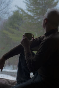 Side view of mature man with coffee sitting on window sill