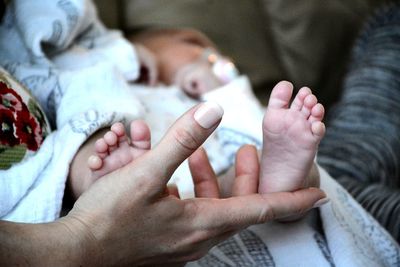 Midsection of woman touching baby leg on bed