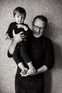 Grandfather with beard and glasses with his grandson sitting on his hands in the studio