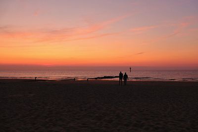 Silhouette people on beach against sky during sunset