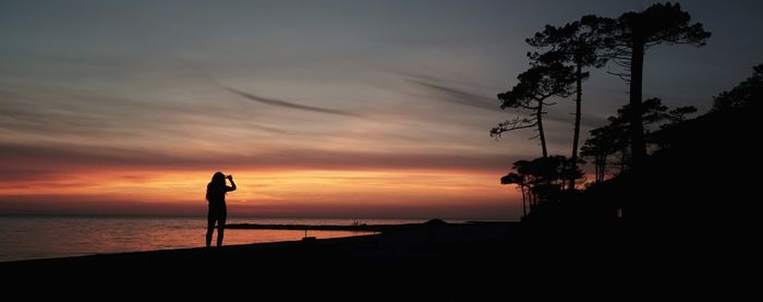 Silhouette person standing on beach against sky during sunset