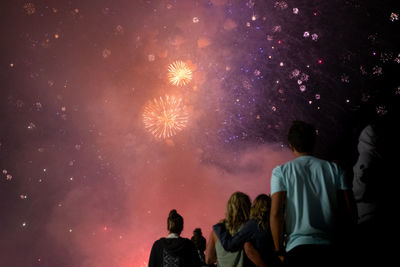 Rear view of people looking at fireworks against sky