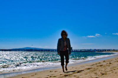 Full length of man standing on beach against clear blue sky