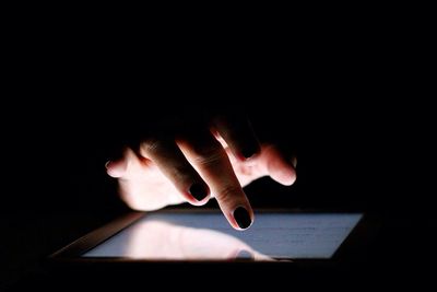 Cropped image of female hand touching digital tablet over black background