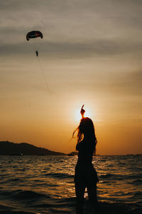 Girl pointing at the paraglide in the sky at the sunset in summer. silhouette of people concept.