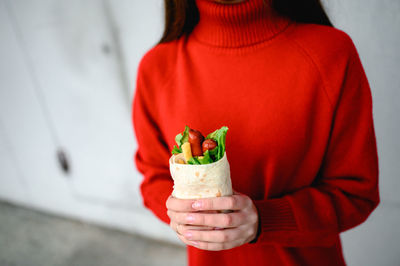 The hands of a girl in red clothes are holding fast street food. shawarma is food in pita