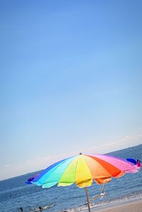 Tilt shot of seagull flying by colorful umbrella at beach against sky