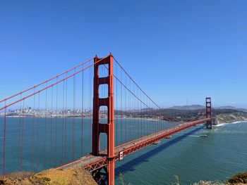 Suspension bridge over sea against clear blue sky