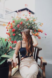 Young woman sitting on chair against plants