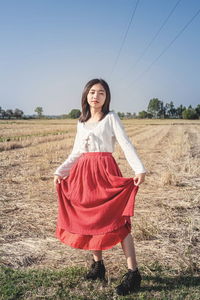 A beautiful woman in a red dress stands among the grasslands and blue sky.