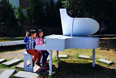 Boy and girl playing piano while sitting on bench against trees