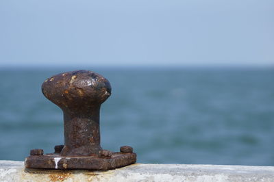 Close-up of rusty metal by sea against clear sky