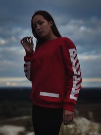 Portrait of beautiful young woman standing on beach against sky