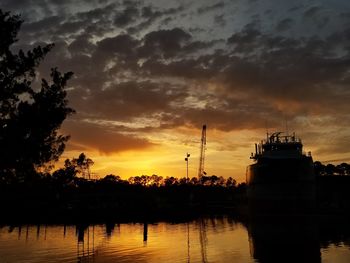 Silhouette trees by lake against orange sky