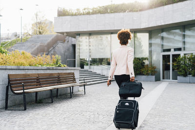 Businesswoman walking with luggage on footpath