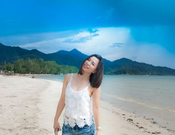 Portrait of smiling mid adult woman standing on beach against blue sky