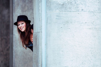 Portrait of smiling woman peeping against wall