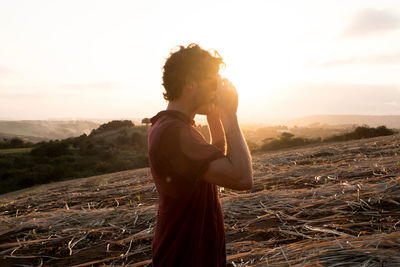 Side view of a young woman standing against sunset