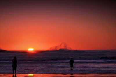 Two silhouette people walking on beach at sunset