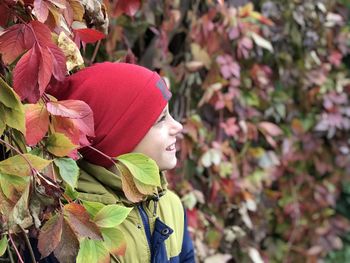 A boy in a pink hat stands on a background red autumn leaves of wild grapes and smile 