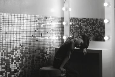 Side view of young man sitting on wall at home