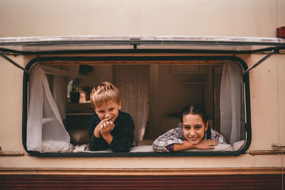 Two happy smiling kids brother and sister look out the window of the camping trailer