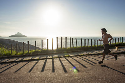 Man running on street by sea against sky during sunny day