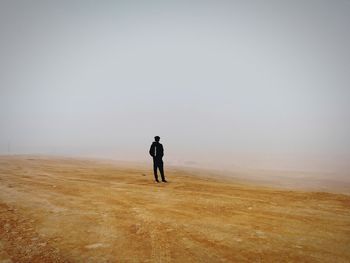 Rear view of man walking on field against clear sky