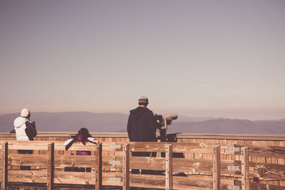 Rear view of people standing by binoculars against sky