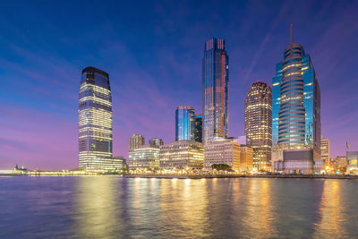 Illuminated modern buildings in city against sky at night