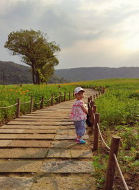 Side view portrait of girl standing on footpath amidst green field