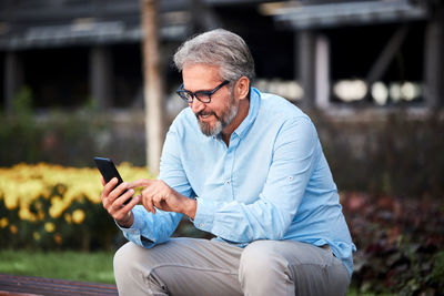 Smiling businessman using mobile phone while sitting in park