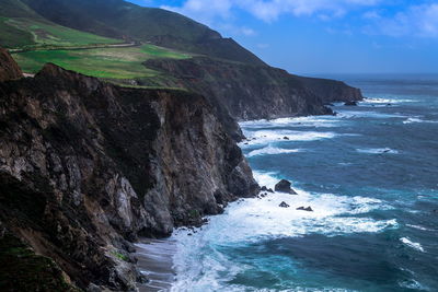 Scenic view of sea by rocky mountains against sky