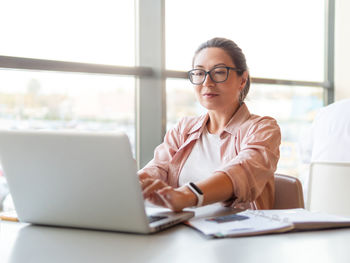 Woman in eyeglasses works with laptop. modern office with panoramic windows at co-working center. 