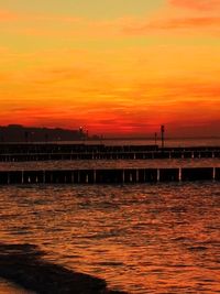 Pier over sea against orange sky
