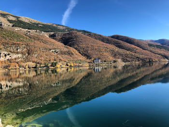 Scenic view of lake by mountain against blue sky