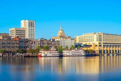 Buildings by river against clear blue sky