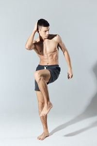 Full length of shirtless man exercising against white background