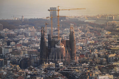 Under construction sagrada familia amidst buildings in city during sunset