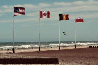 American, canadian and flags on beach against sky