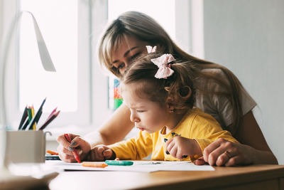 A young mother teaches her little daughter to draw with colored pencils. time together, creativity