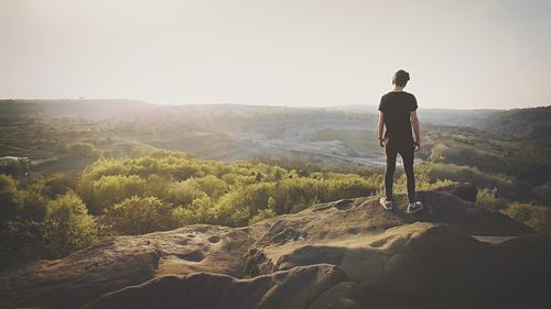 Rear view of man standing on rock by landscape against sky