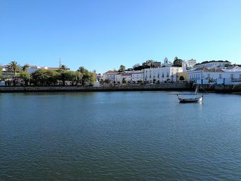 Sailboats in river by buildings against clear blue sky