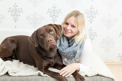 Portrait of smiling woman with dog relaxing on bed at home
