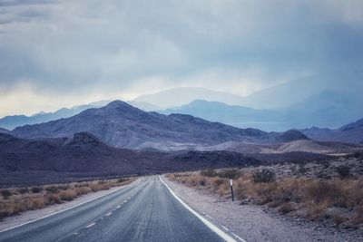 Road leading towards mountains against sky