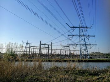 Low angle view of electricity pylon on field against clear sky