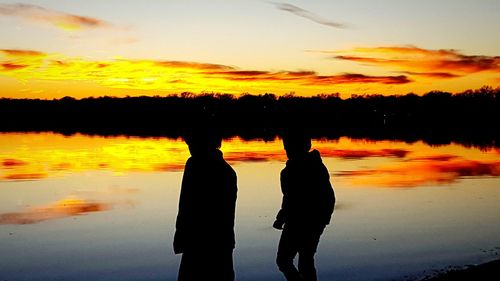 Silhouette couple standing on shore against sky during sunset