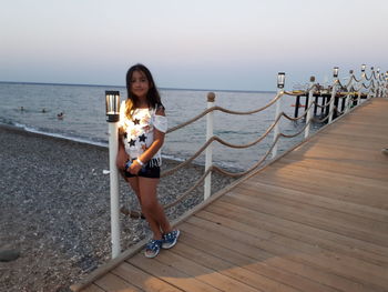 Woman standing on railing by sea against sky