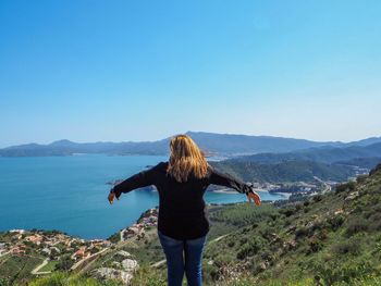 Rear view of woman standing on mountain against clear blue sky